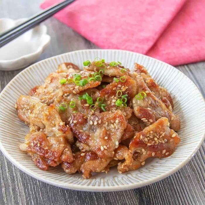 お皿に盛られた焼肉の料理。ゴマとネギがトッピングされ、食欲をそそる見た目です。背景に箸と赤い布が置かれています。