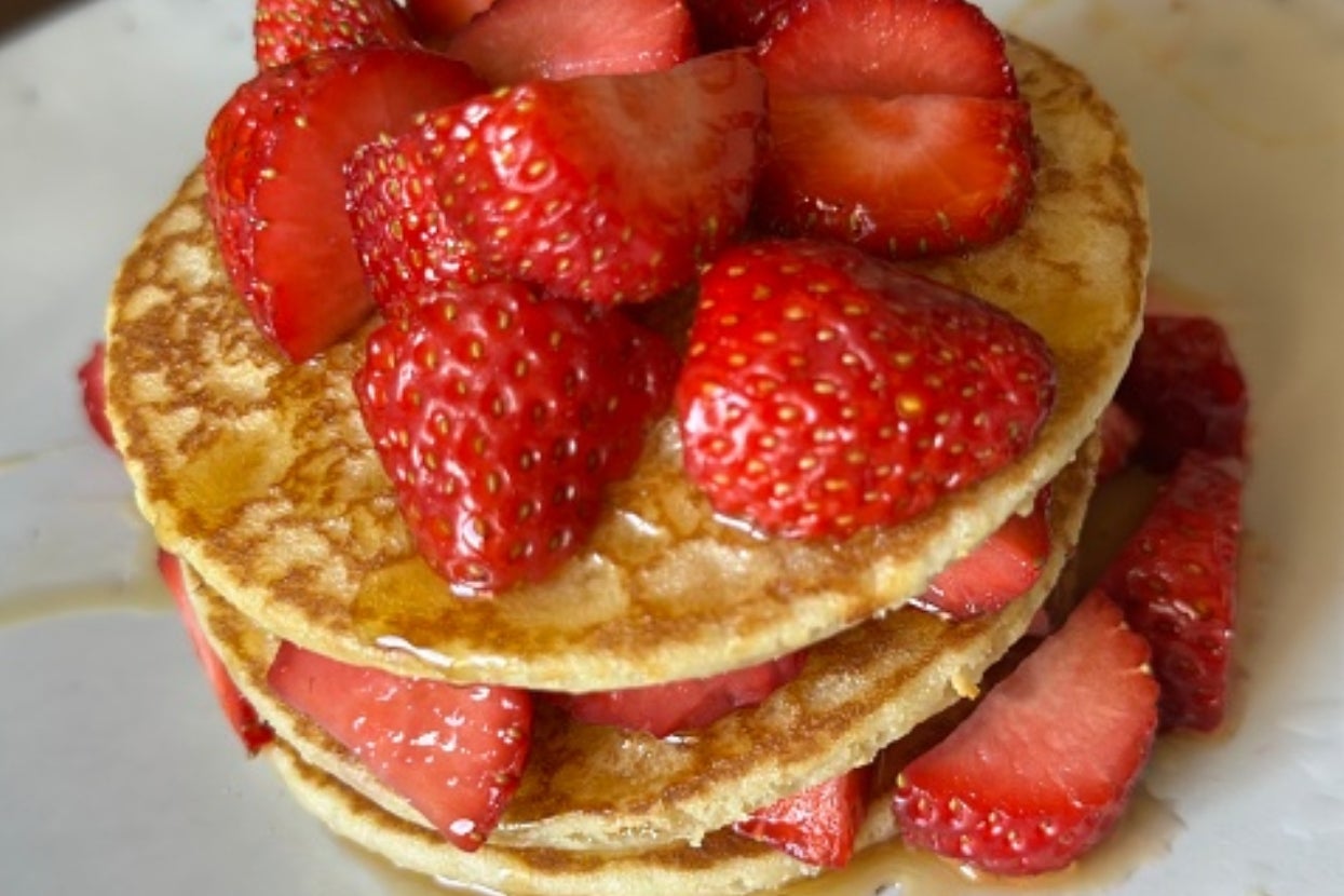 Stack of pancakes topped with sliced strawberries and a drizzle of syrup on a white plate