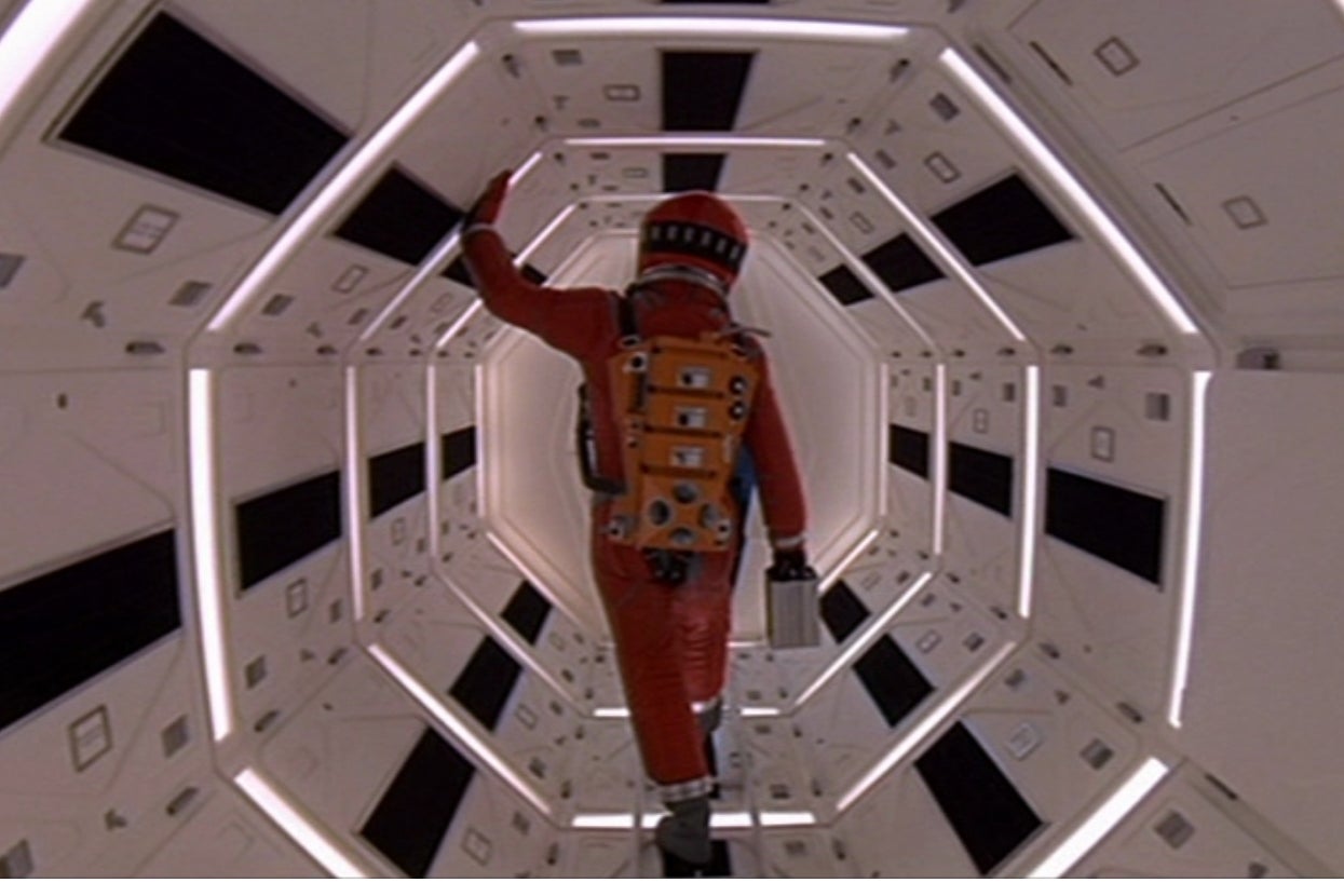 An astronaut in a space suit walks down a geometric, futuristic corridor, holding a case, evoking a sci-fi atmosphere