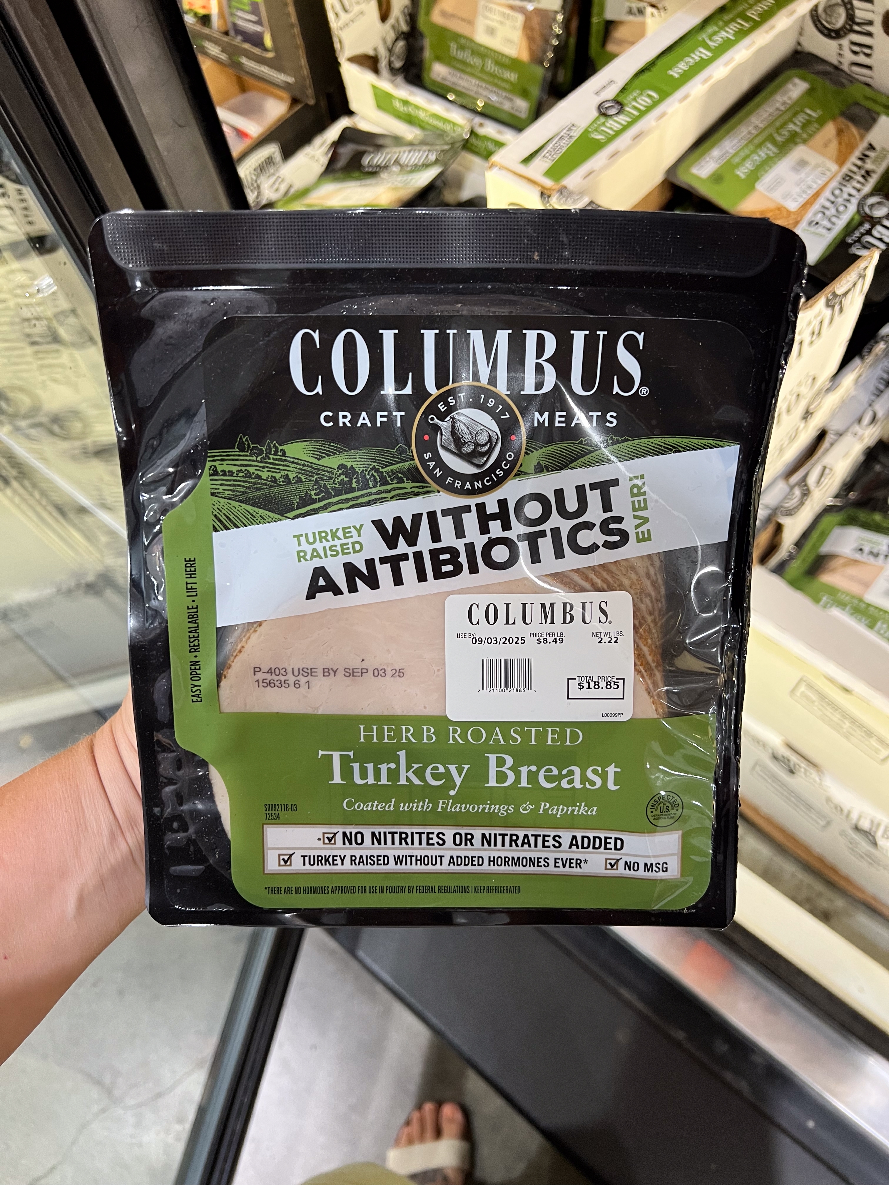 Package of Columbus herb roasted turkey breast, without antibiotics, shown in a person's hand at a store