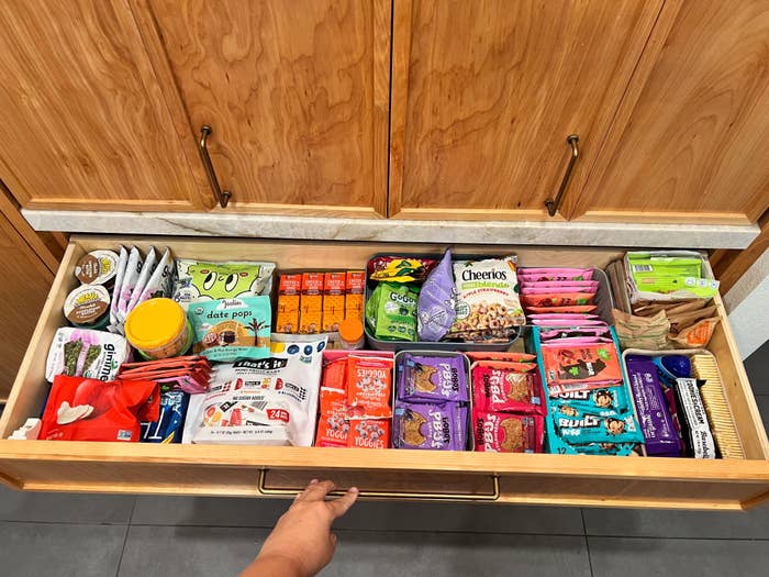 Hand opening a well-organized snack drawer with various packaged snacks including crackers, fruit bars, and chocolate