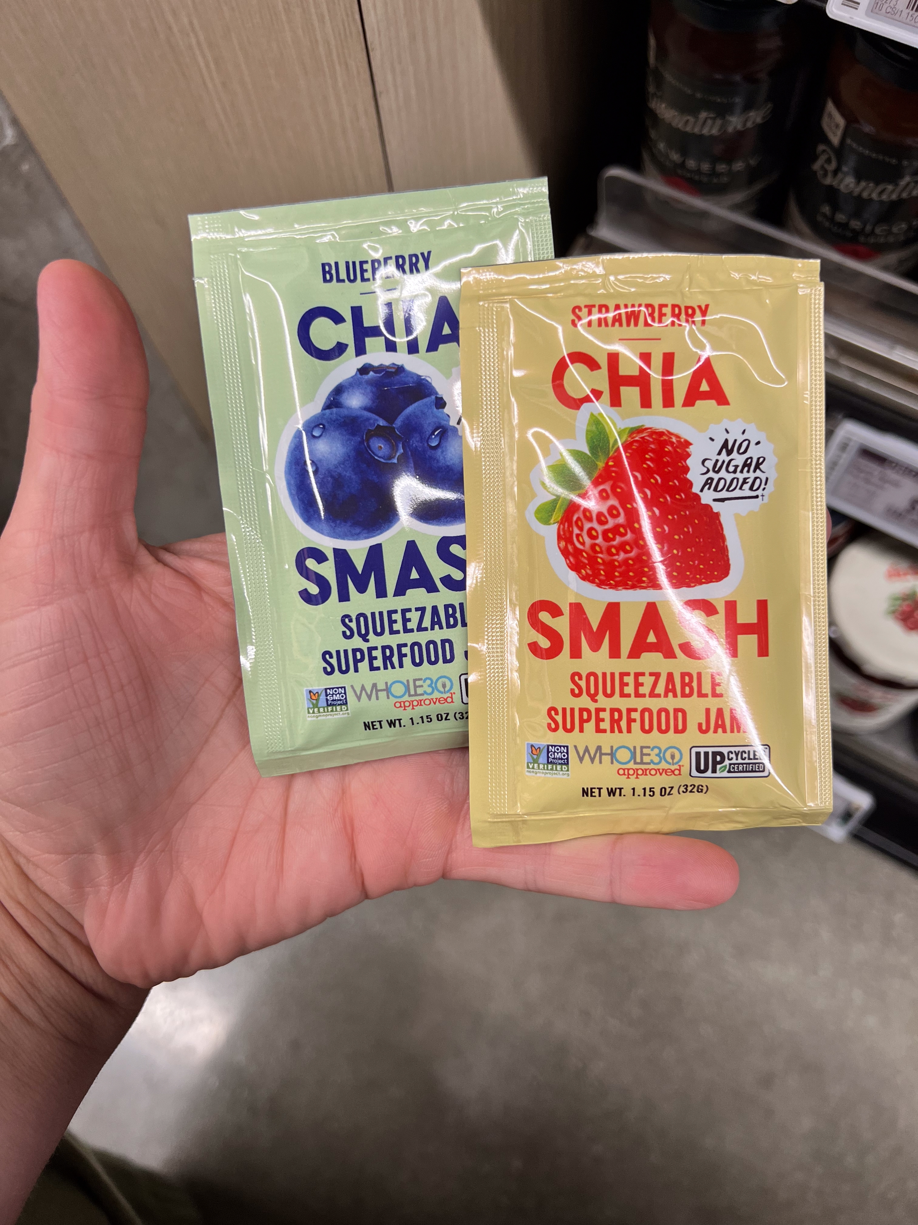 Hand holding blueberry and strawberry chia jam packets labeled "Chia Smash" with "No Sugar Added" text