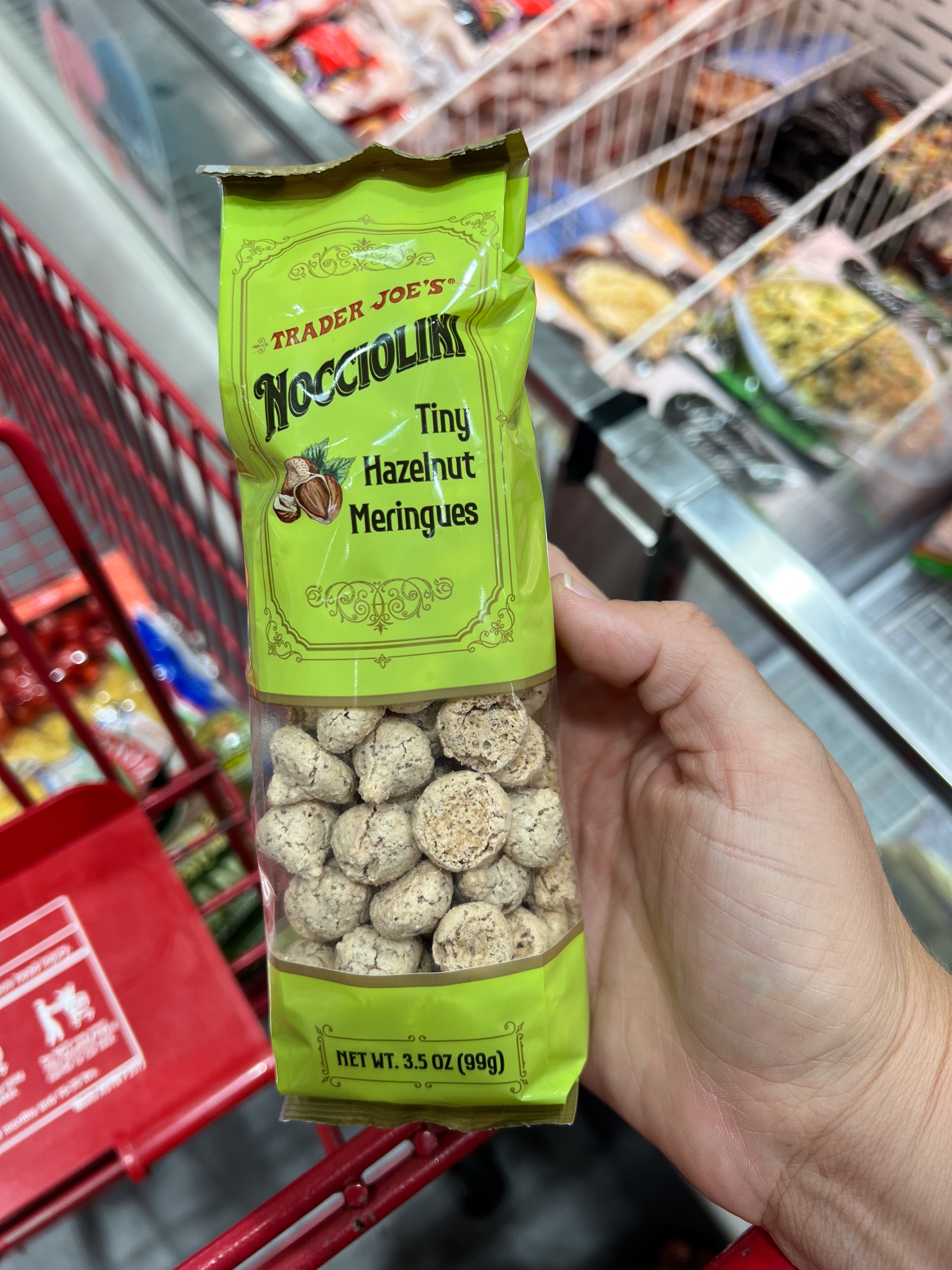 Bag of Trader Joe's Nocciolini Tiny Hazelnut Meringues held in a hand above a shopping cart