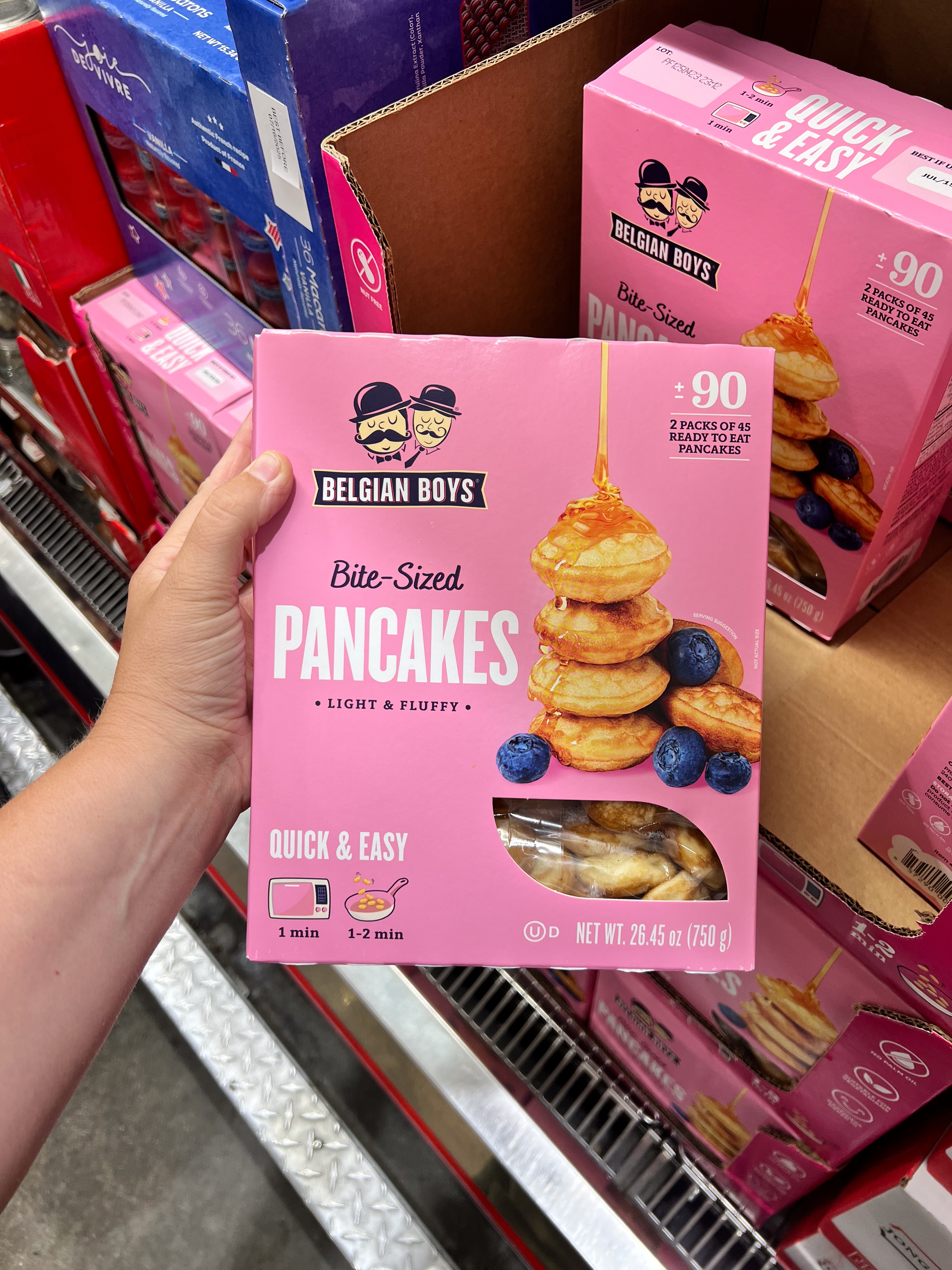 Hand holds a box of Belgian Boys Bite-Sized Pancakes. Package states "light & fluffy," "quick & easy," and contains blueberries and pancakes image