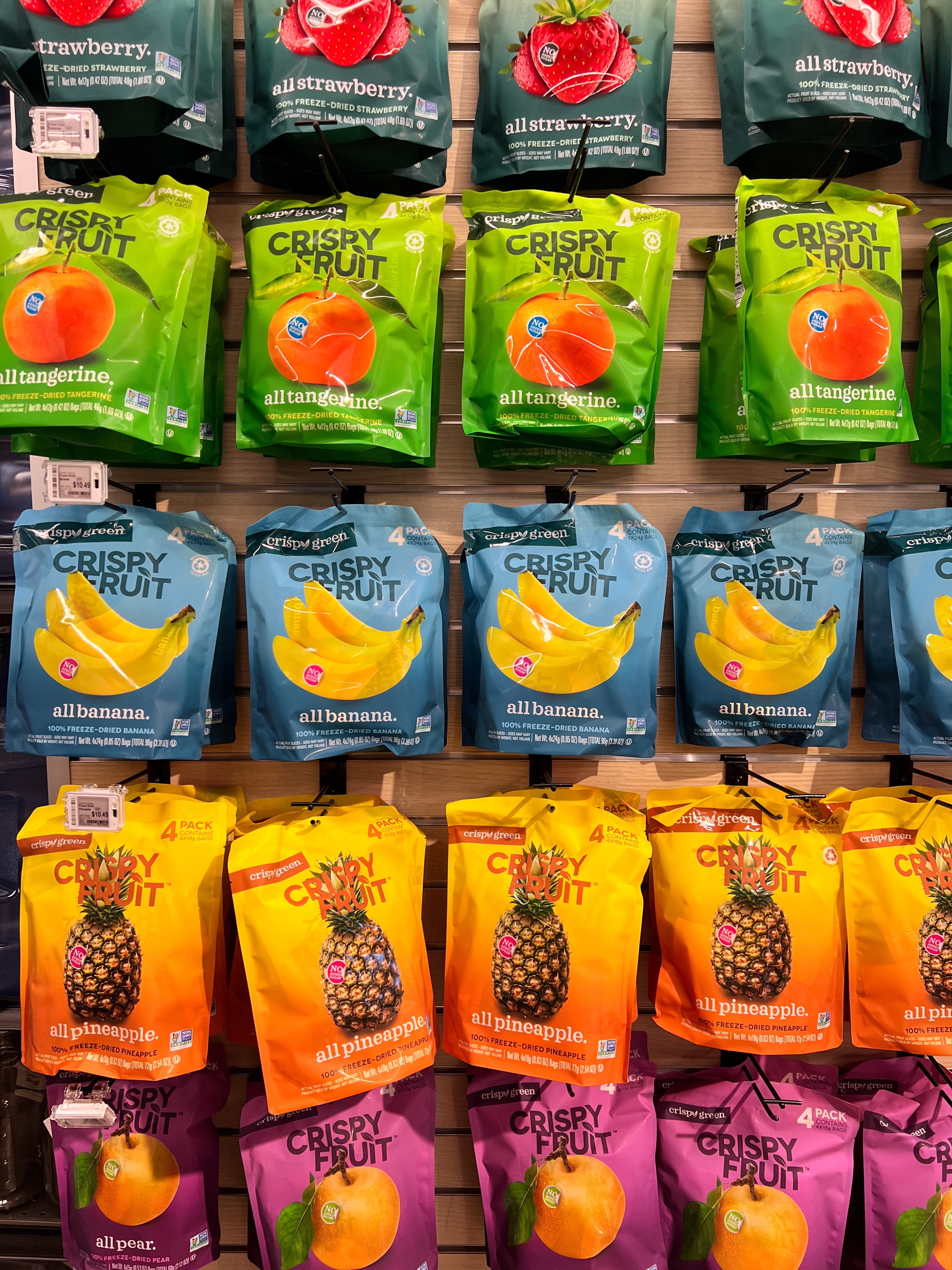 Various bags of dried fruit snacks displayed on a shelf, featuring flavors like tangerine, banana, pineapple, and pear