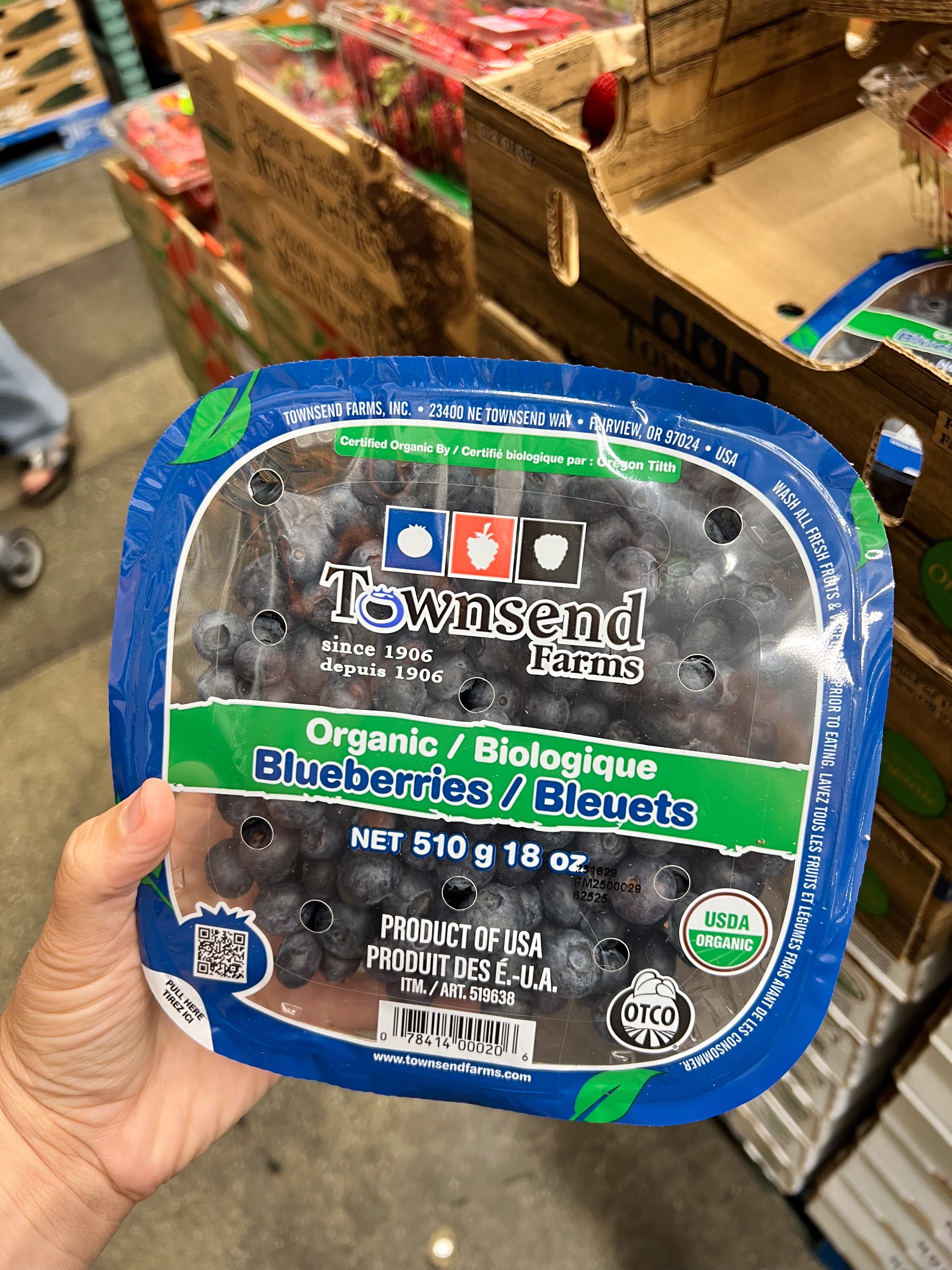 A hand holds a package of Townsend Farms organic blueberries in a store. The label shows the weight as 510g or 18oz