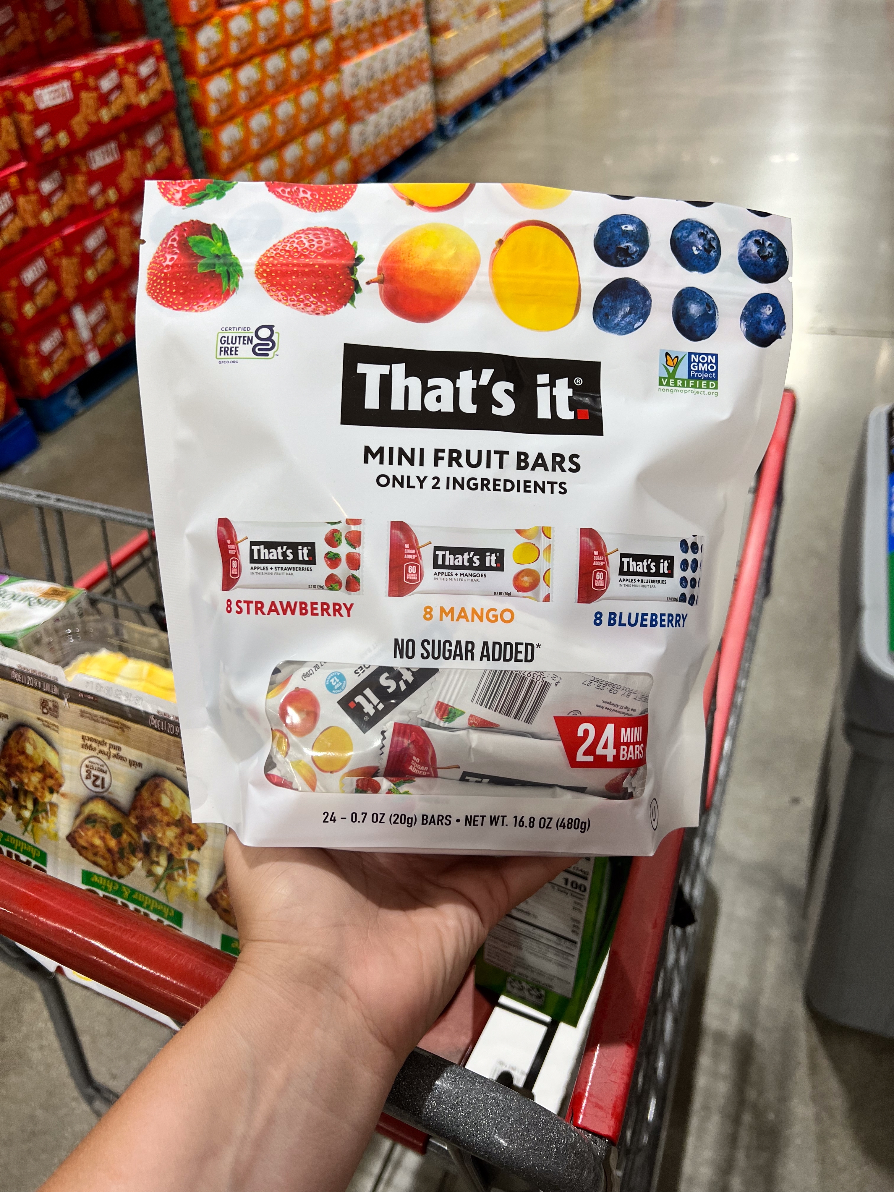 Person holding a pack of "That's it" mini fruit bars in a store aisle, showcasing fruit illustrations and flavors like strawberry, mango, and blueberry