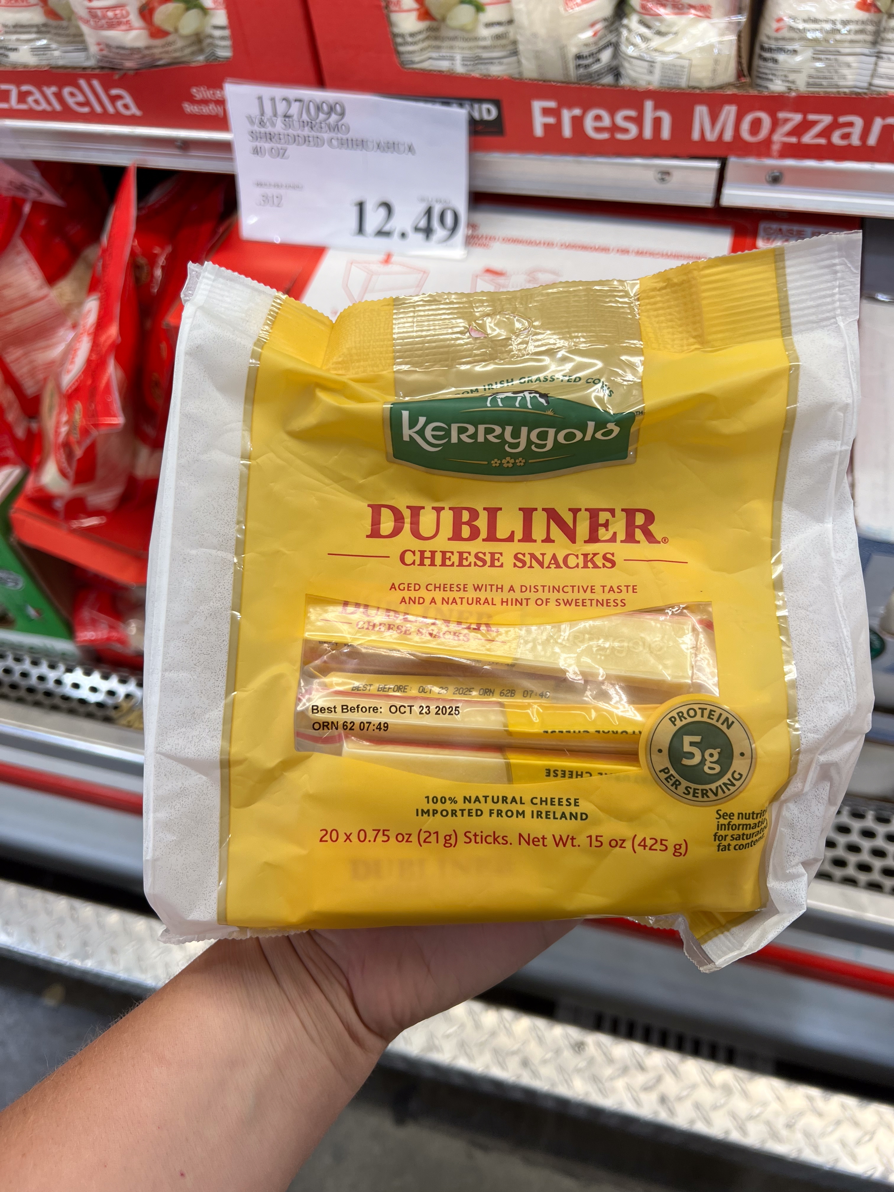 Pack of Kerrygold Dubliner Cheese Snacks held in hand at a store, labeled with price. Cheese is described as aged with a hint of sweetness