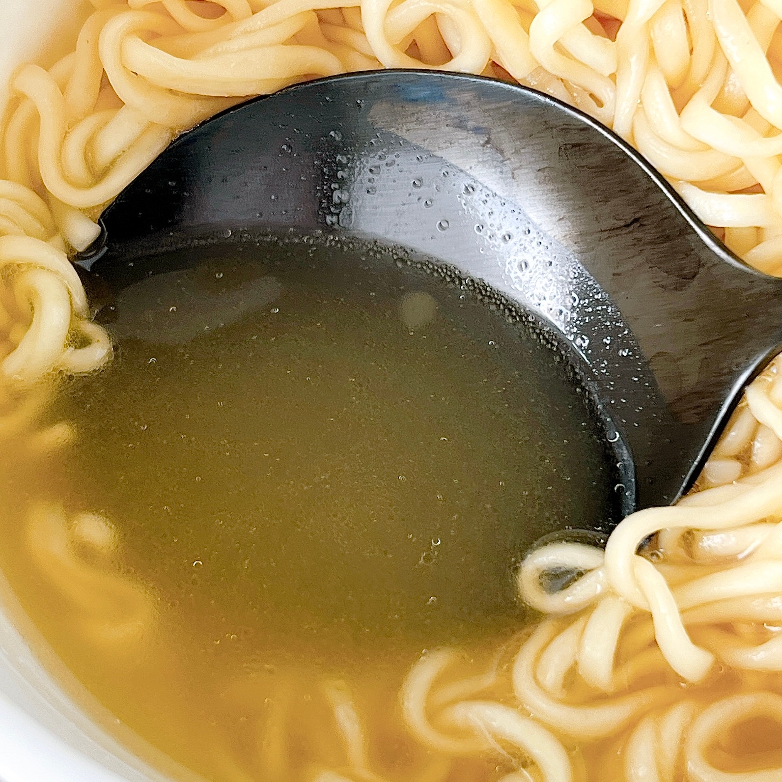 ラーメンのスープをすくう黒いレンゲと麺が映ったクローズアップ写真。