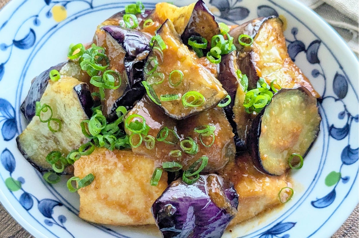 揚げなすと豆腐の炒め物が白い皿に盛られ、上には細かく刻んだネギがトッピングされています。