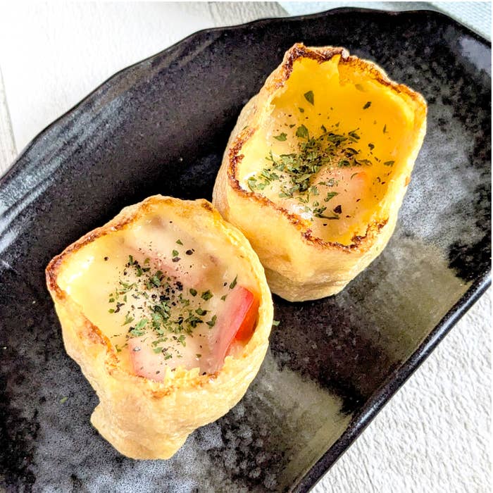 焼かれた油揚げのカップにチーズとトマト、ハーブが入った料理が黒いお皿に2つのっている。