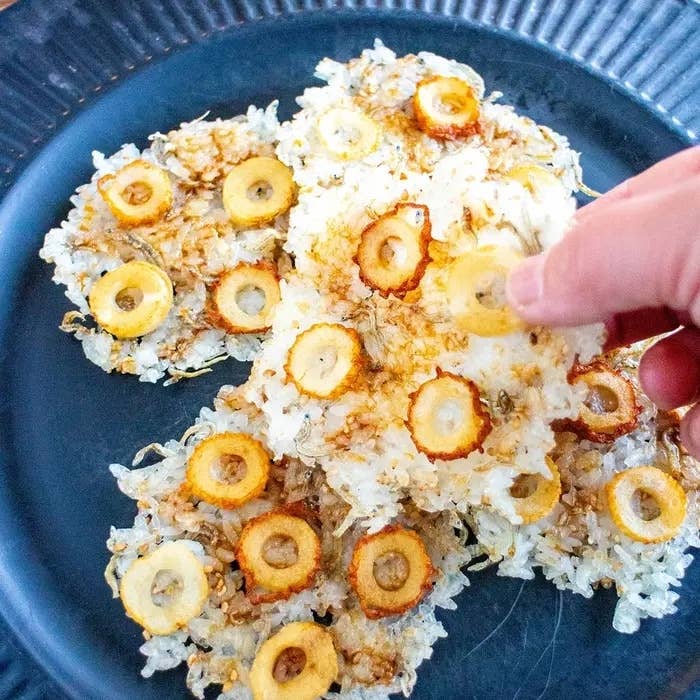 大根の薄切りがのった焼きおにぎりが皿に盛られ、手で1つ持ち上げられています。