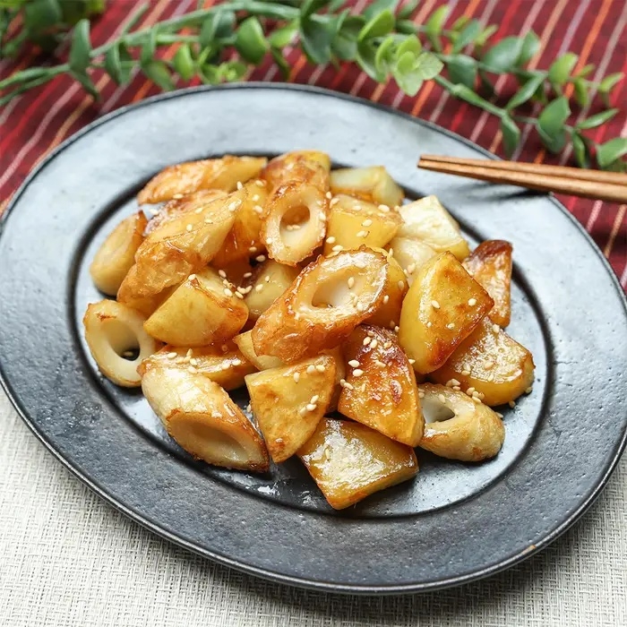 黒い皿に盛られた焼きちくわとじゃがいも、ゴマがトッピングされています。テーブルに箸が置かれています。