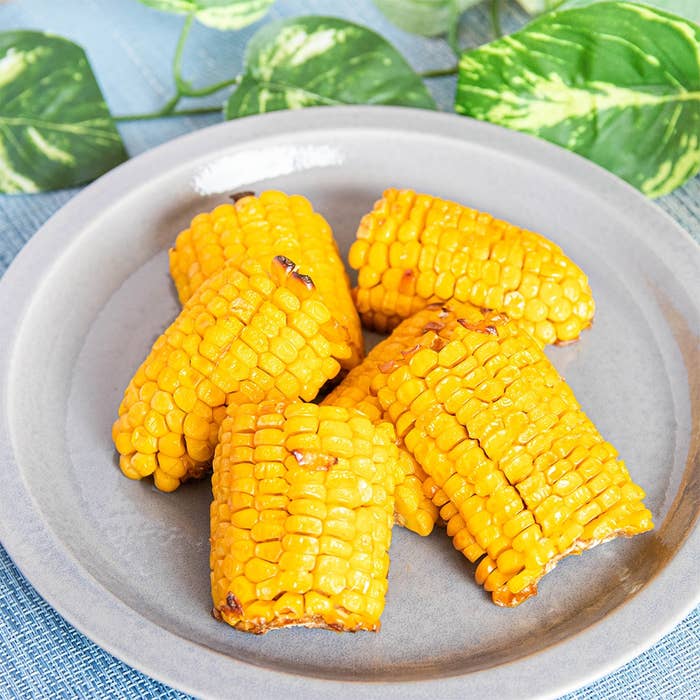 お皿に盛られた焼きとうもろこしが置かれている。背景には緑の葉が見える。