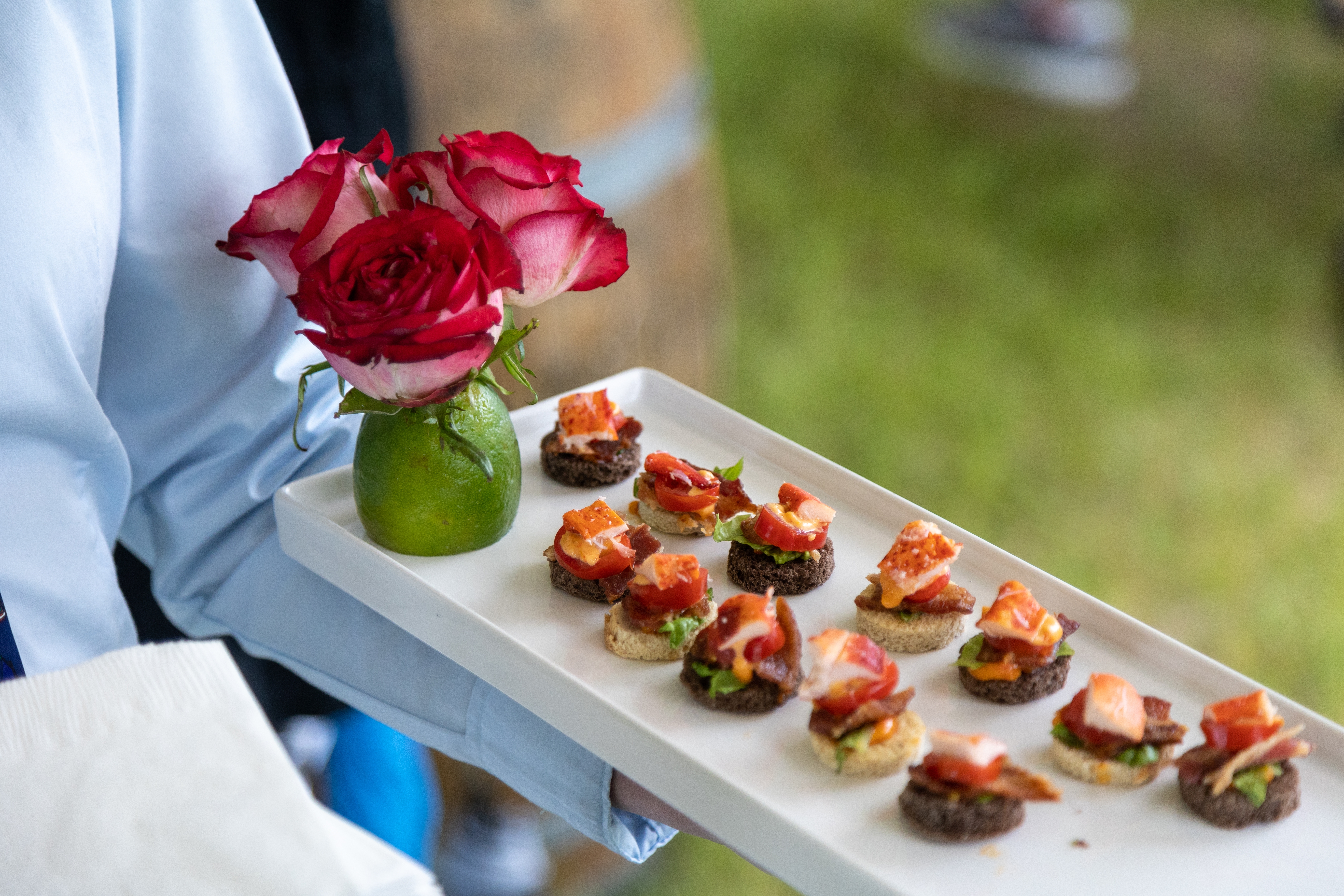Tray with assorted appetizers topped with bacon and small vase of roses in background