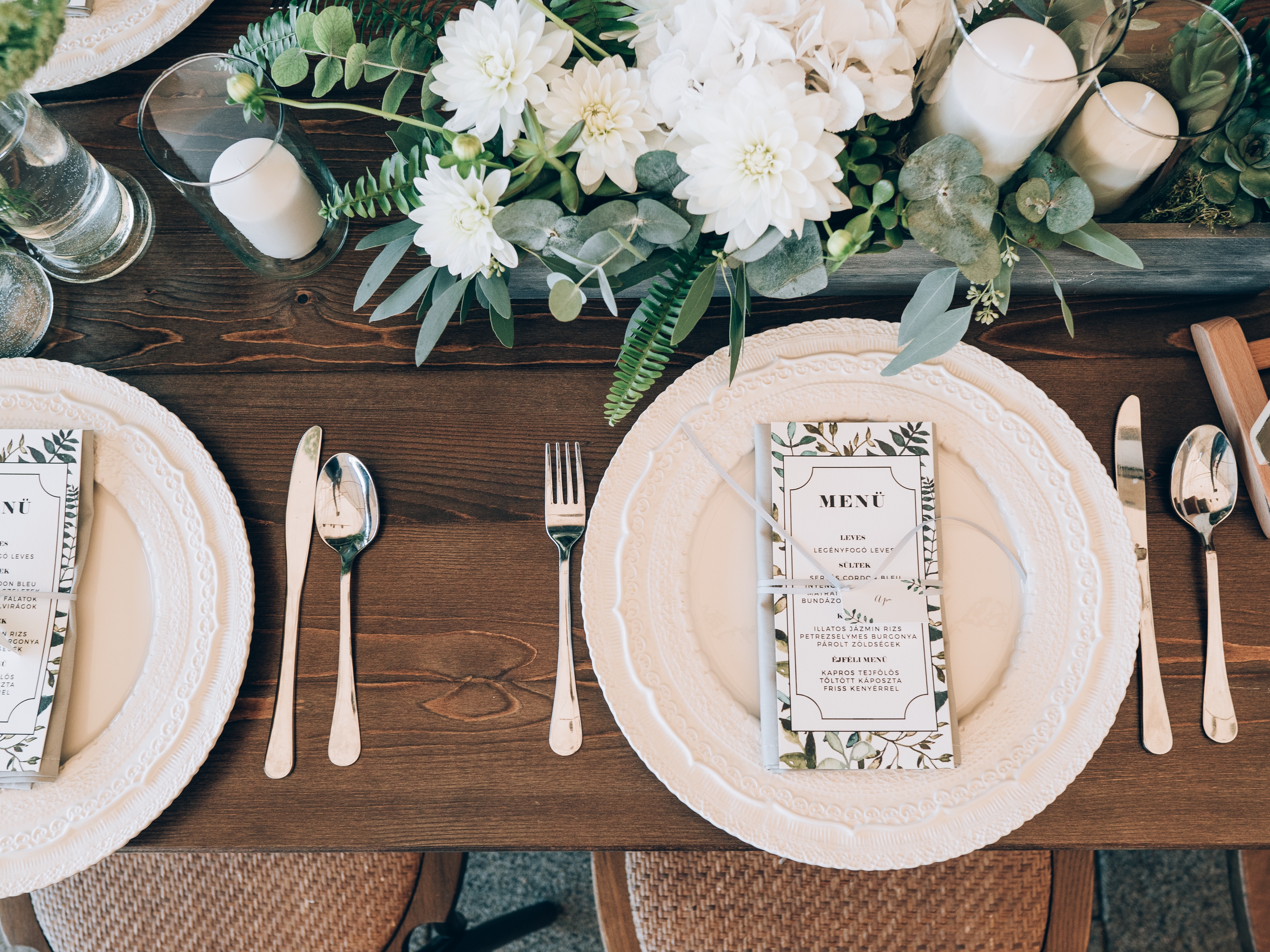 Elegant table setting with floral centerpieces, white plates, menu cards, and silverware neatly arranged on a wooden table