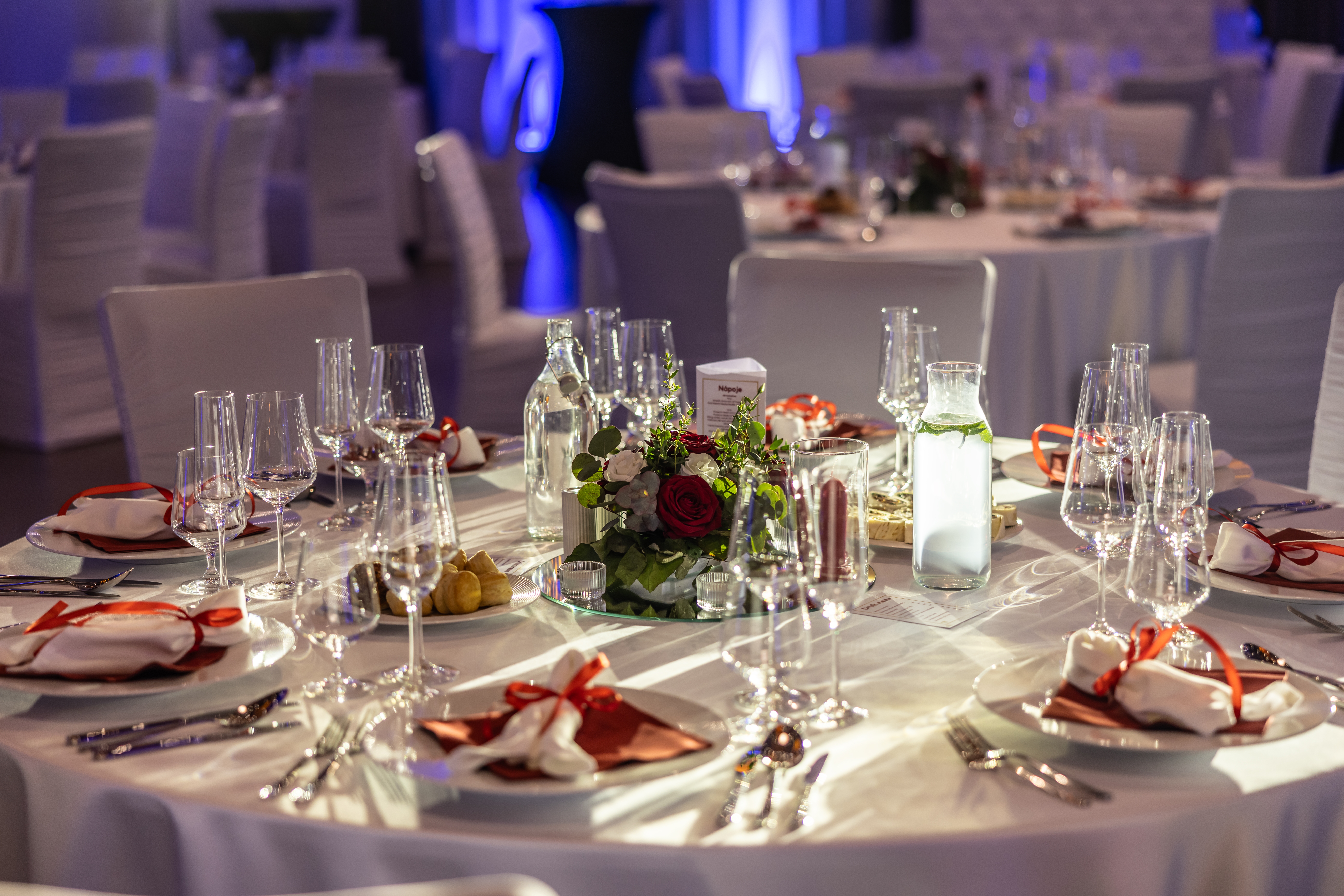 Elegant banquet table with white tablecloths, neatly arranged glassware, floral centerpiece, and place settings for a formal event