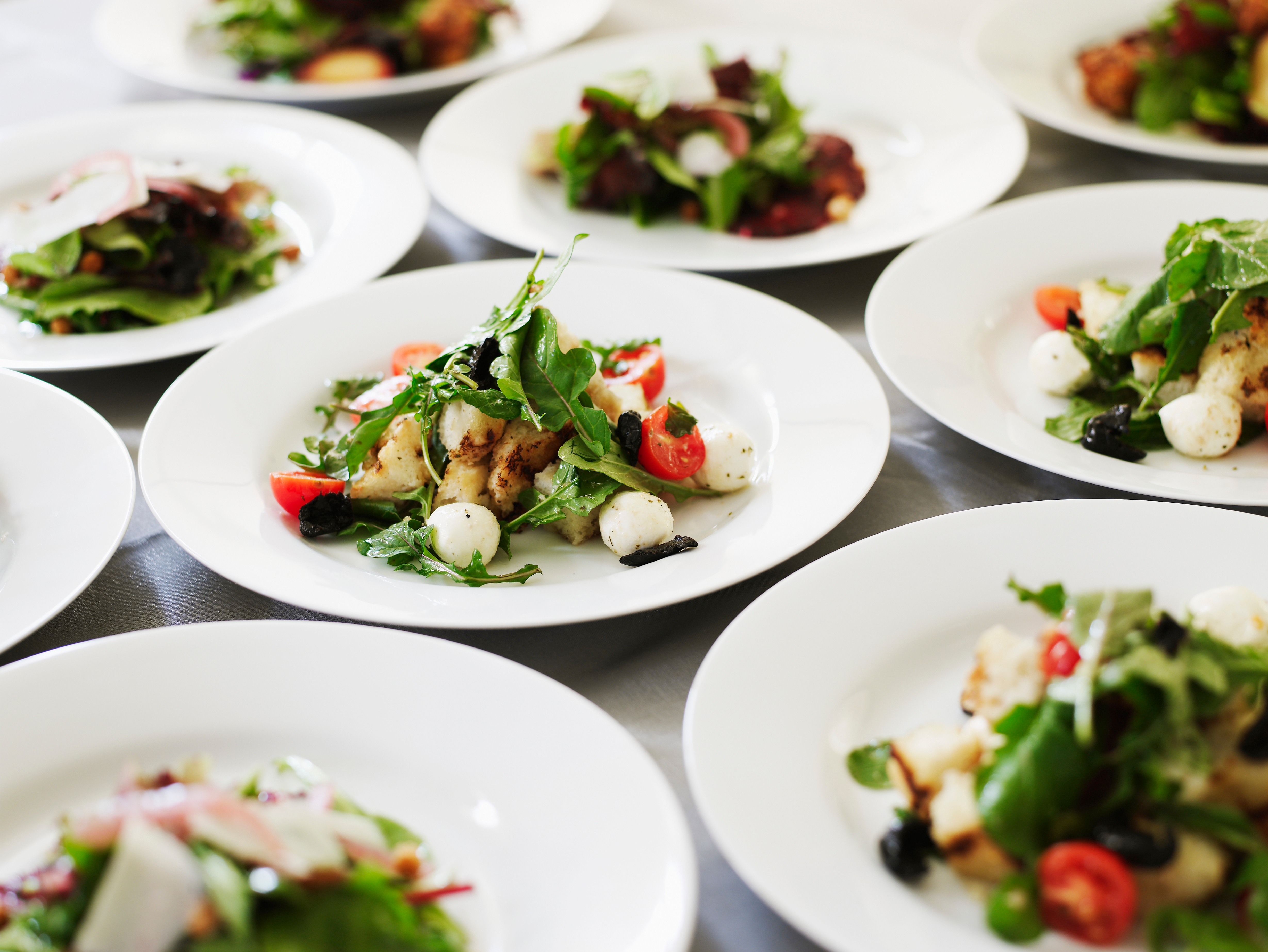 Plates of gourmet salads featuring mixed greens, cherry tomatoes, and mozzarella balls neatly arranged on a dining setup