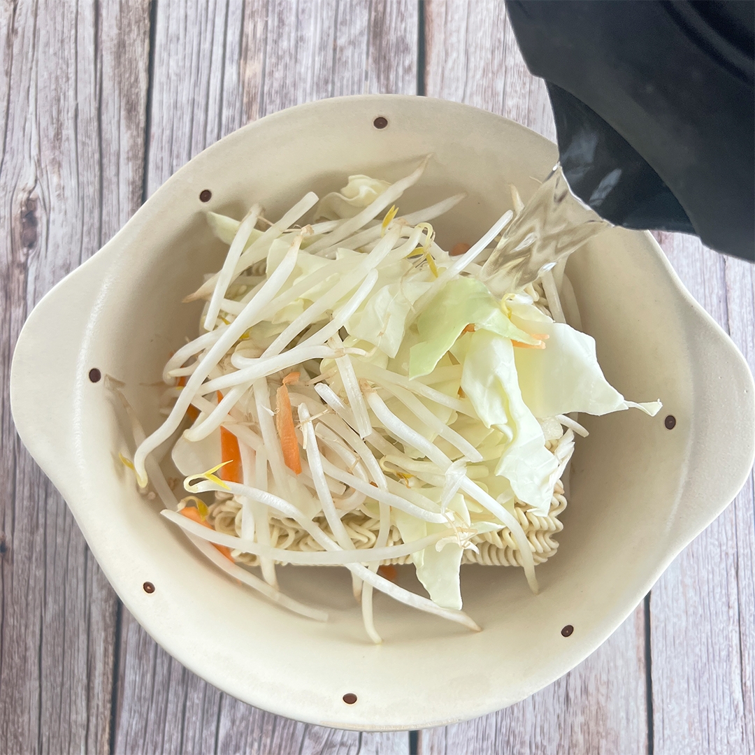 ボウルにインスタントラーメン、もやし、キャベツが入り、お湯が注がれている。