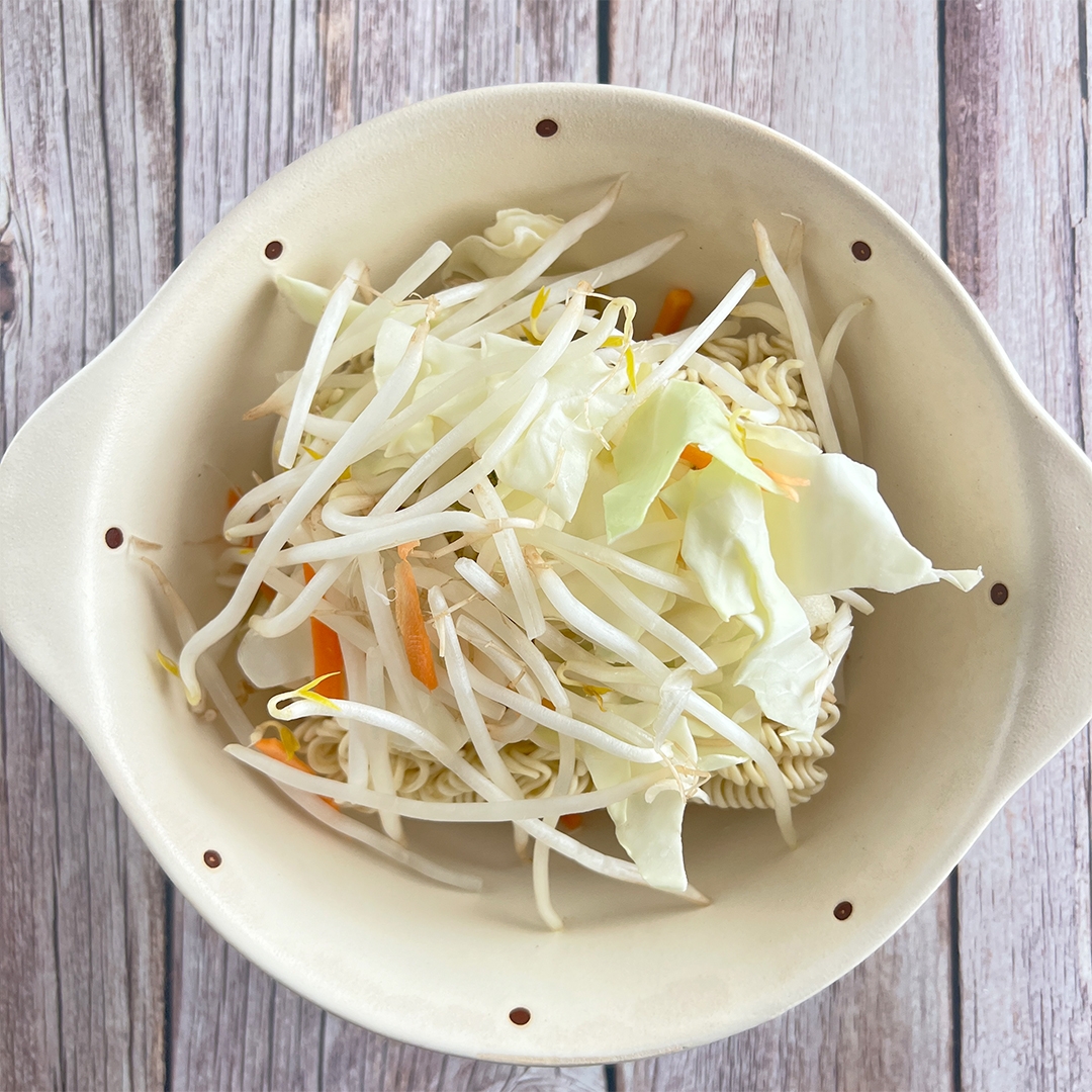 ボウルにインスタント麺とモヤシ、キャベツが盛られた料理。