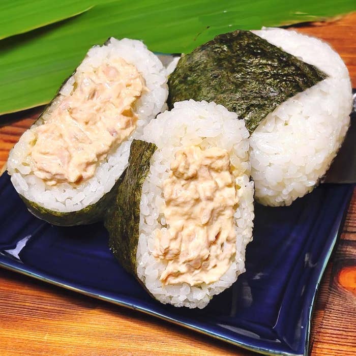 皿に盛られたツナマヨおにぎりのクローズアップ。のりで包まれたご飯が分かれて、具材が見えている。