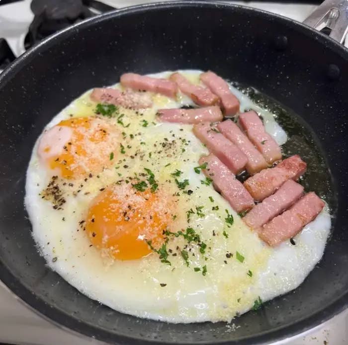 フライパンで目玉焼きが調理され、上にパセリと胡椒が振りかけられている。
