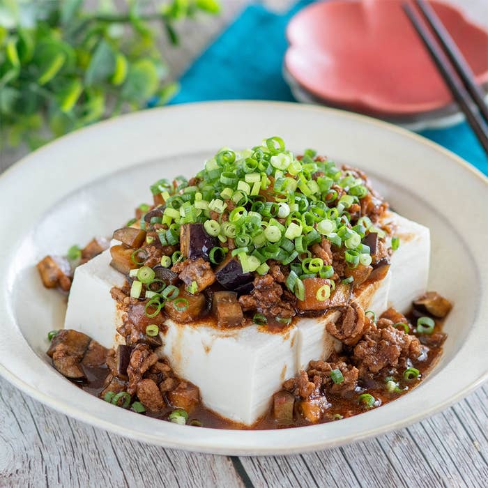 豆腐の上にひき肉とネギが盛られた料理。食器、ナプキン、箸が並んでいる。