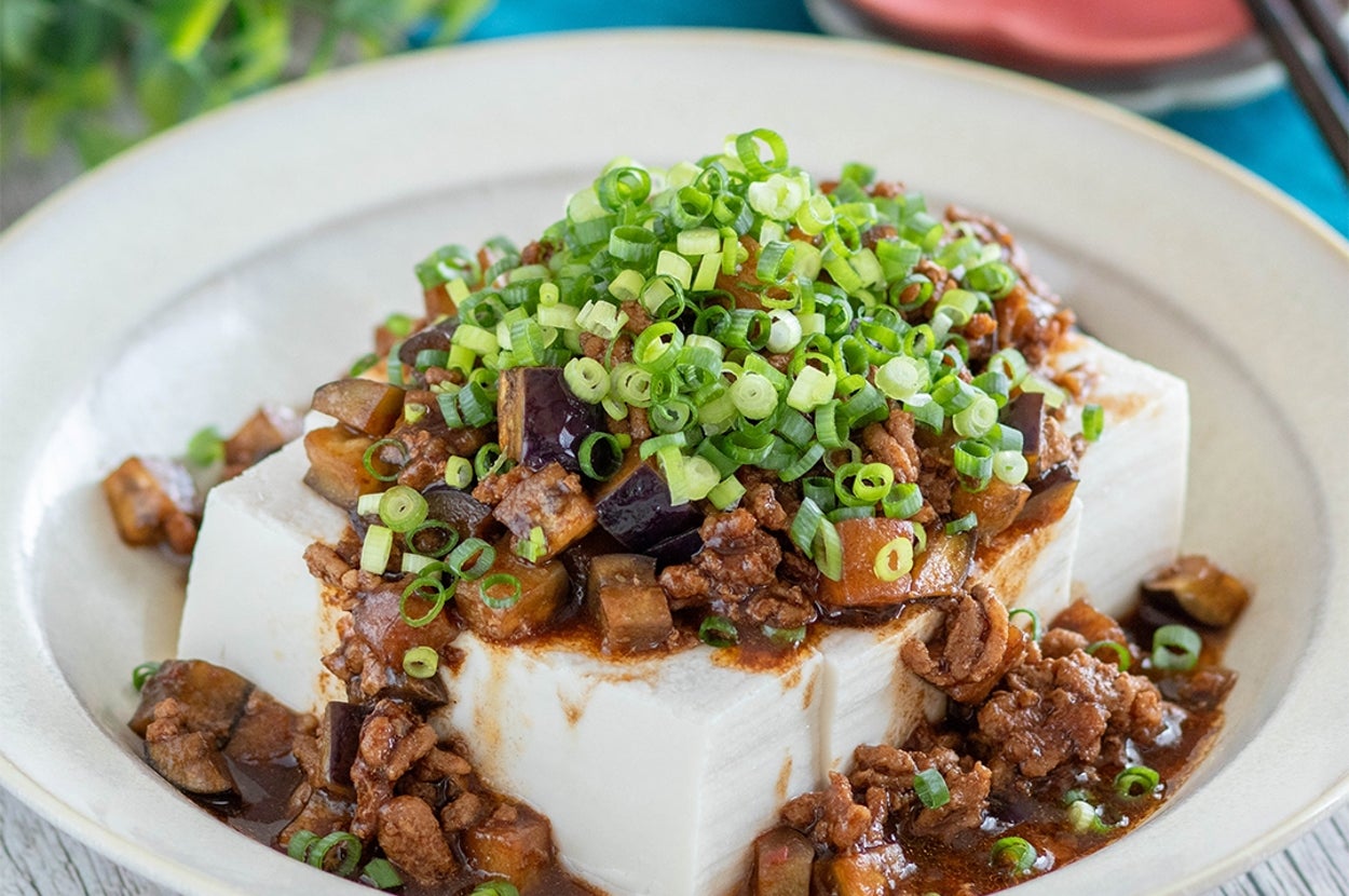 皿に盛られた麻婆豆腐、刻んだネギがたっぷり。テーブルには箸と小皿が置かれている。