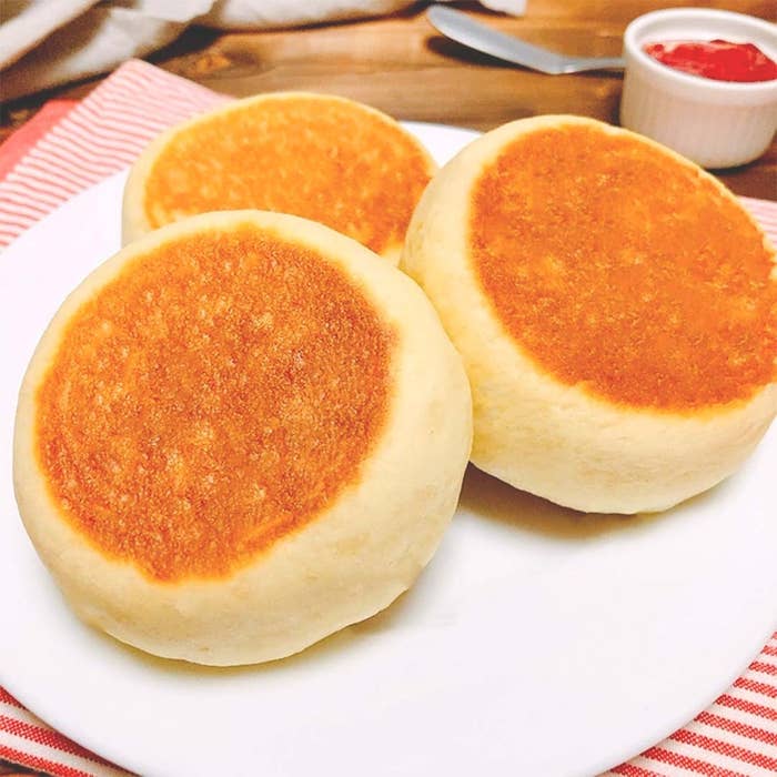 白い皿にふっくら焼き上がった3つのパンケーキが載っている。背景に小さなジャムの入った容器が見える。
