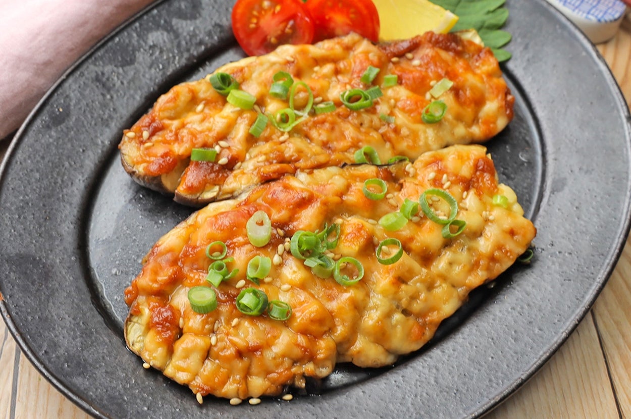 ナスにチーズとトマトが載った焼き料理。刻んだネギが散らされています。 chắn