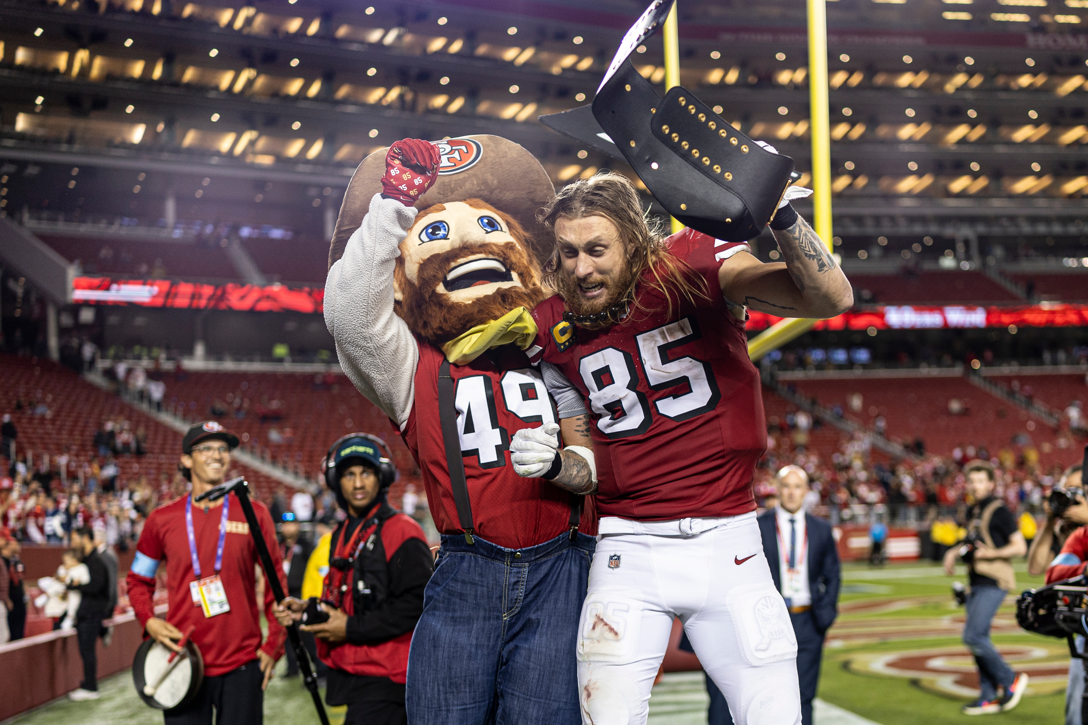 Football player celebrates on field with mascot, holding a championship belt