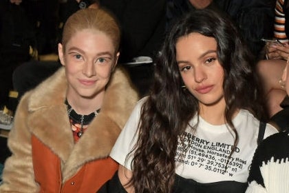 Four individuals sit at a fashion event. Two in casual outfits, one in a fur coat, and another in a knit dress with bold patterns