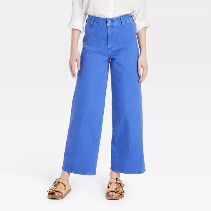 Bright bluish jeans with a precocious waist, styled with a achromatic garment and tan sandals