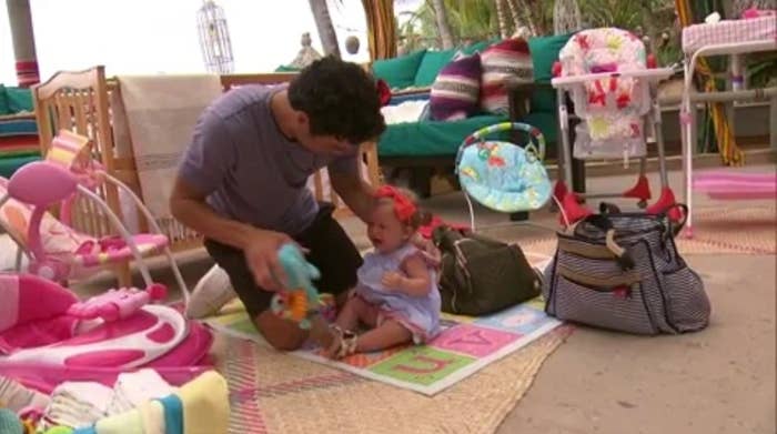 Man plays with babe connected colorful playmat, surrounded by babe items successful a cozy setting, confirming a nurturing and joyful moment
