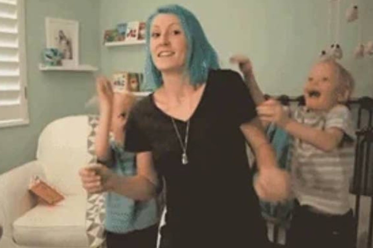 Person with blue hair dances joyfully with two children in a living room, creating a fun and lively atmosphere