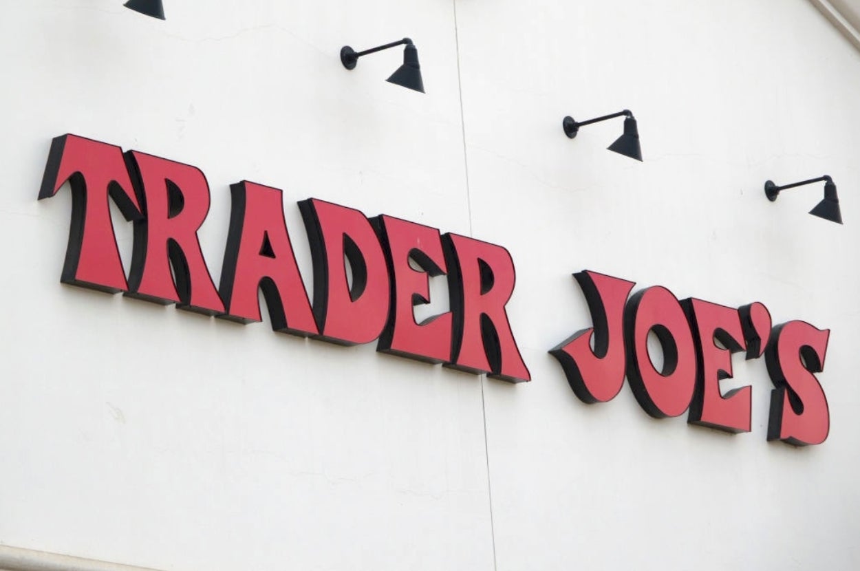 Trader Joe's store sign with bold lettering on a white wall, featuring black light fixtures above