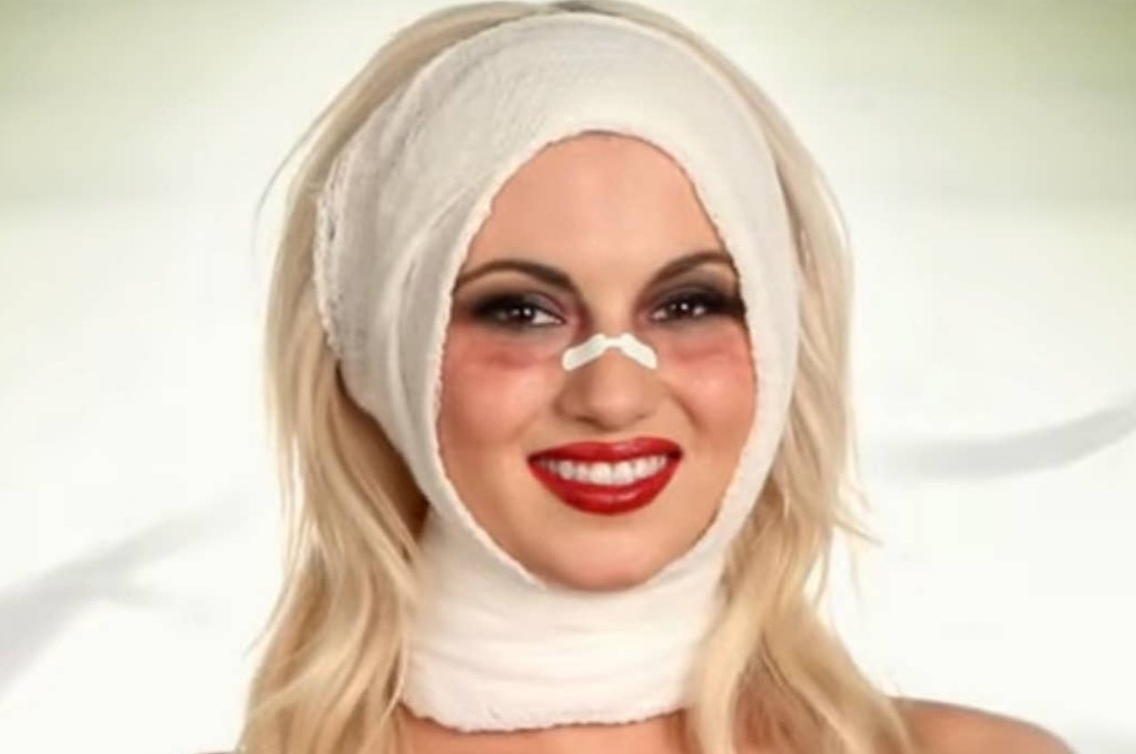 Person smiling with wrapped head and nose bandage, wearing makeup
