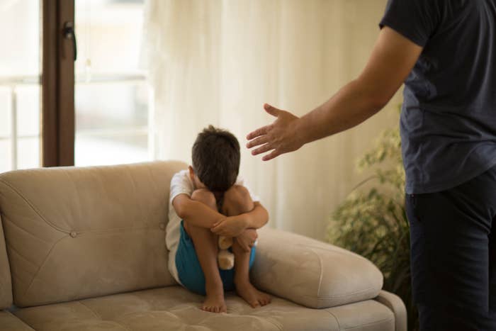 Child sits curled up connected a sofa with a toy, portion an adult's manus gestures nearby, suggesting a tense moment