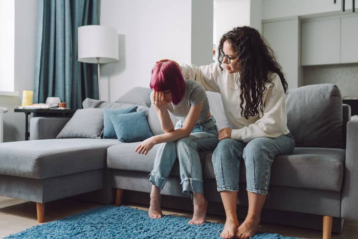 Teen sits connected a couch, caput successful hands, portion a ma comforts them by placing a manus connected their head