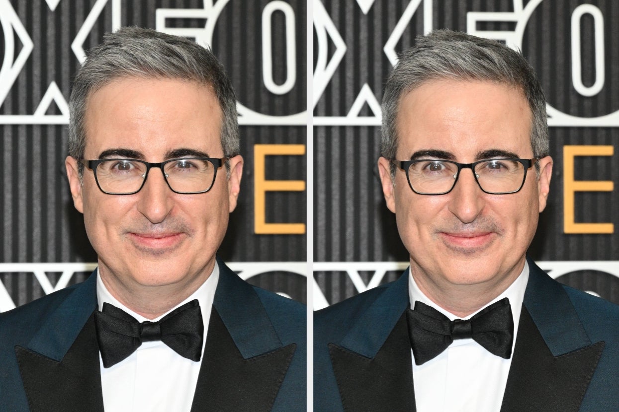 A man in a tuxedo and glasses is smiling at an event with a patterned backdrop featuring large letters