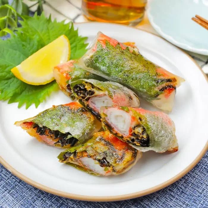 皿に盛られたのりを使った巻き寿司。野菜と魚介類が具材として使われている。背景に青じそとレモンが添えられている。