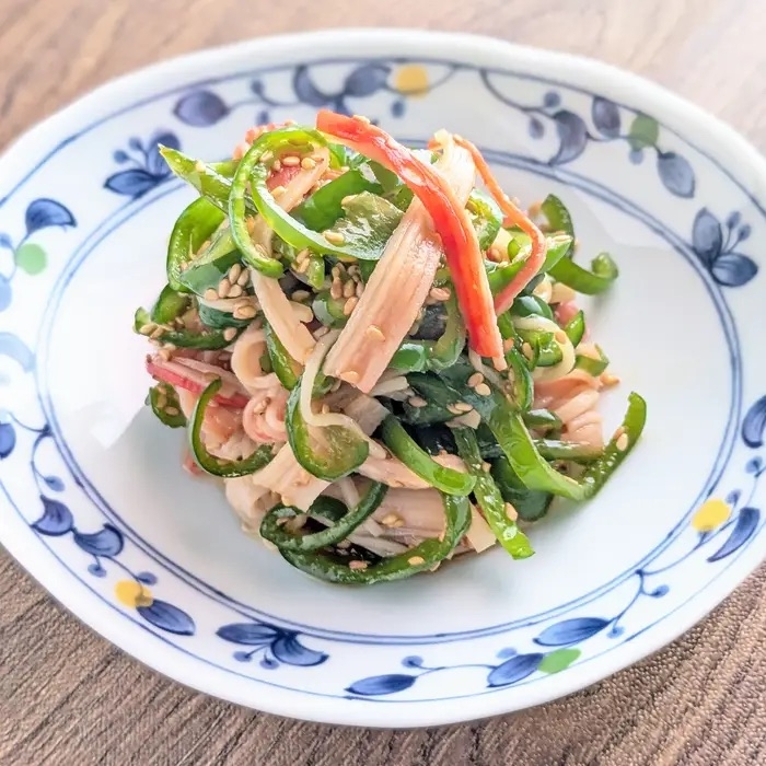 彩り豊かな野菜のサラダ。刻まれたピーマン、カニカマとごまが混ざり、陶器の皿に美しく盛り付けられています。