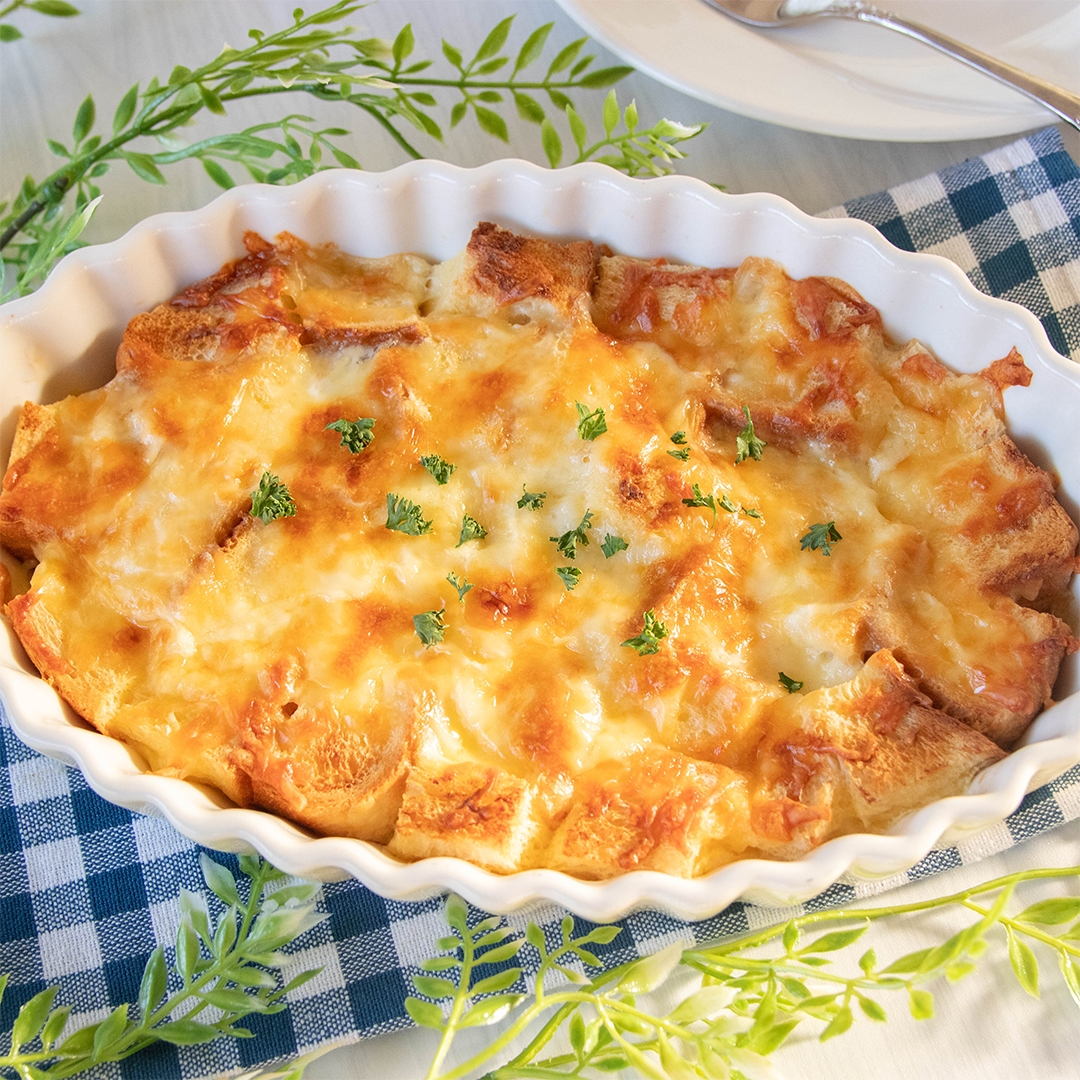 焼きたてのチーズパンプディングが白いオーブン皿に盛り付けられ、青いチェックのクロスの上に置かれています。
