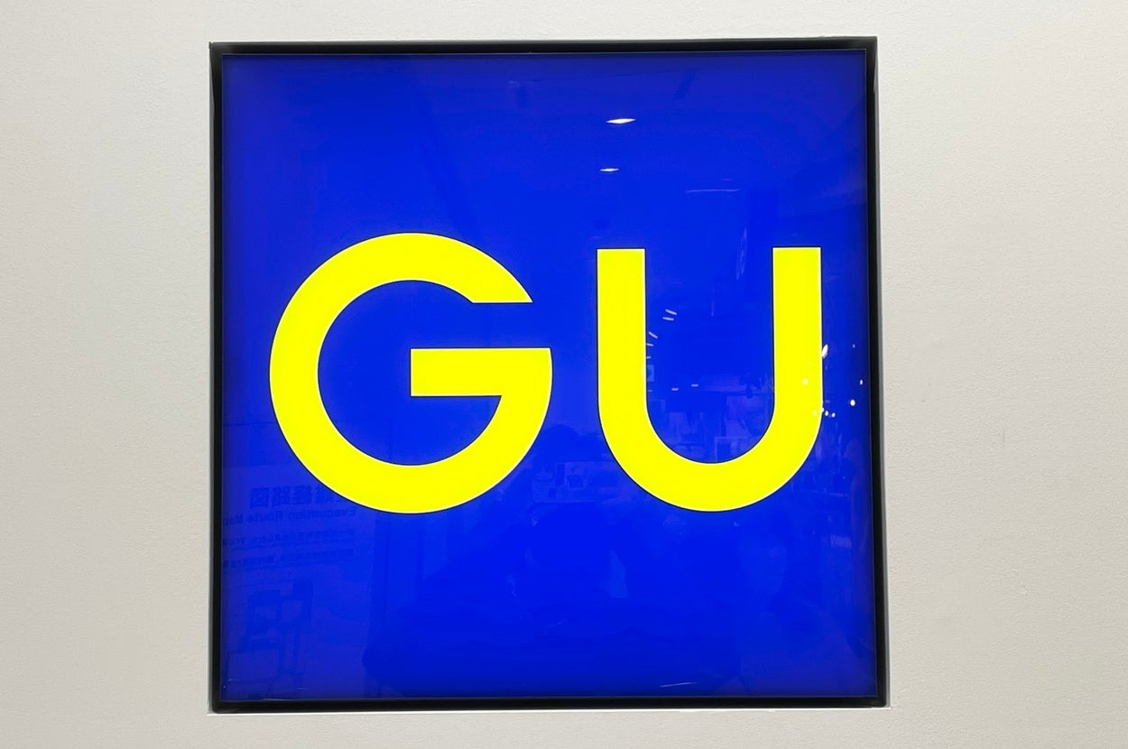 A square sign displaying the large letters "GU" in a bright, clear font