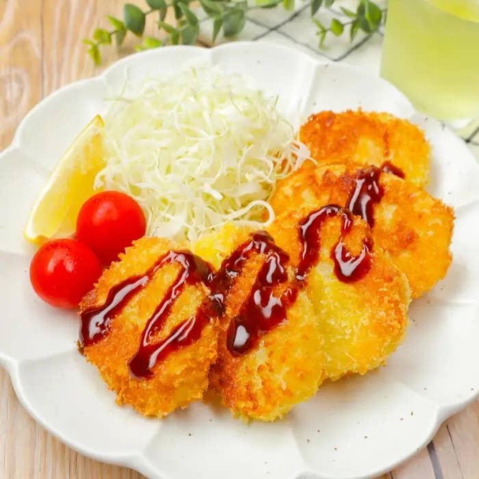 揚げ物のコロッケがソースと共に盛り付けられ、トマト、キャベツの千切り、レモンが添えられた料理。