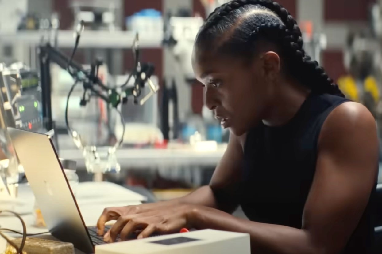 Person intensely working on a laptop in a tech lab, focused amidst equipment and cables