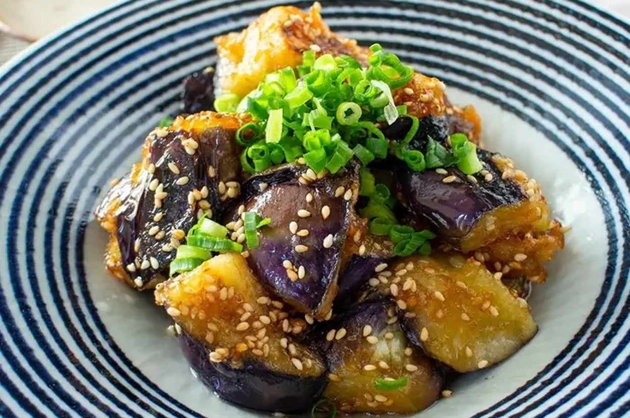 青ねぎとごまがトッピングされた茄子の料理が和風の器に盛られている。