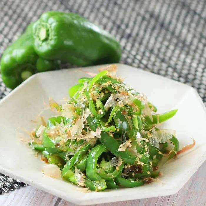 お皿に盛られた薄切りピーマンの和え物。鰹節とゴマがトッピングされた、新鮮な野菜料理。