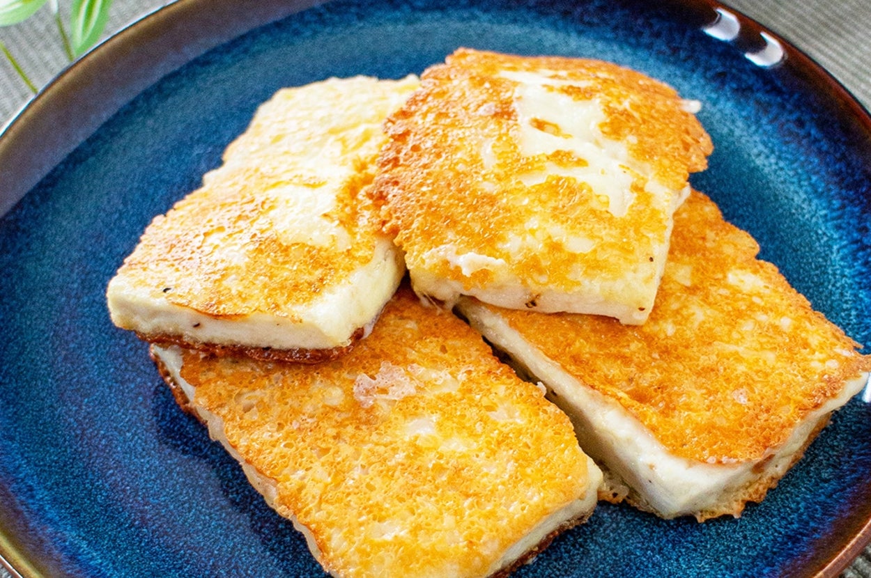 青い皿に盛られたカリッと焼いた豆腐のステーキが並んでいます。背景に植物が少し見えます。