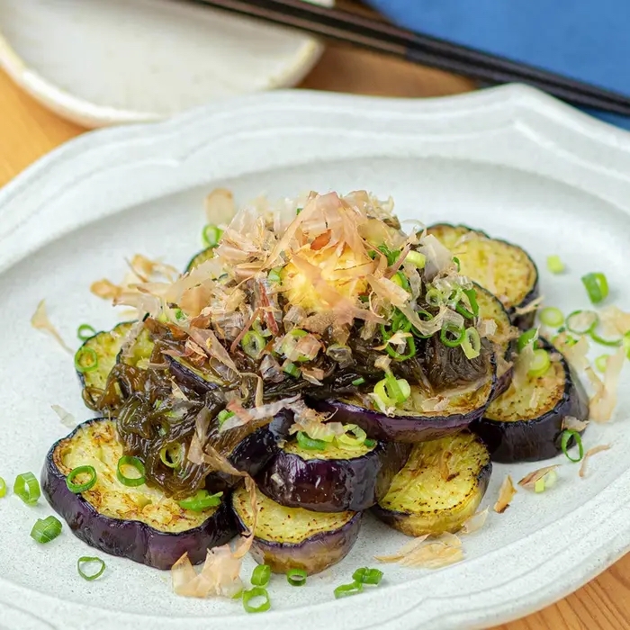 焼きナスが盛り付けられた皿に刻みネギと削り節がトッピングされています。